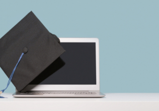 A black graduation cap on the corner of a laptop with a blue background